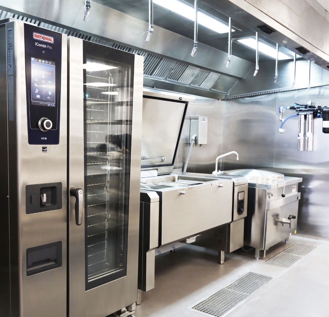 Commercial kitchen equipment line with stainless steel work surfaces and ventilation hood