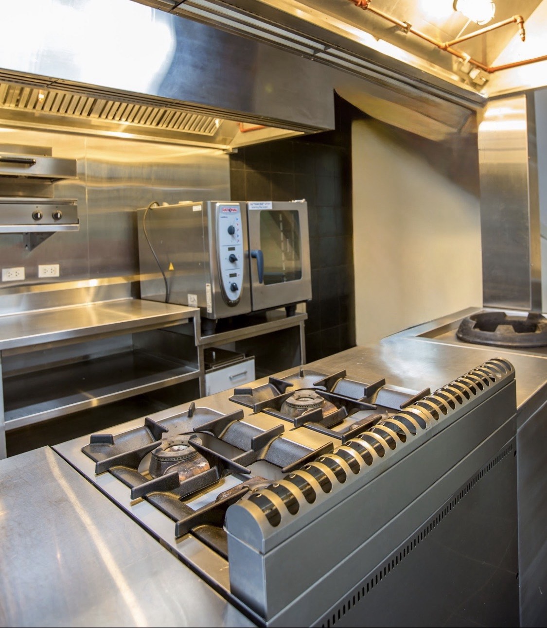 Commercial kitchen cooking equipment with stainless steel work surfaces and ventilation hood