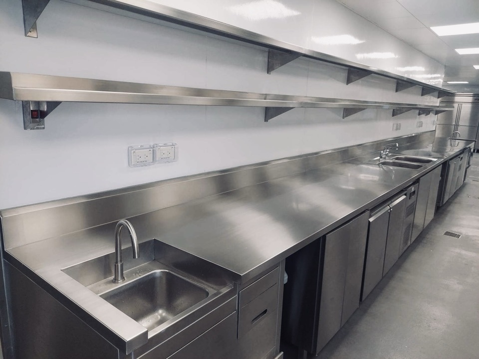 Stainless sink, counter, backsplash, and washing area in a commercial kitchen.